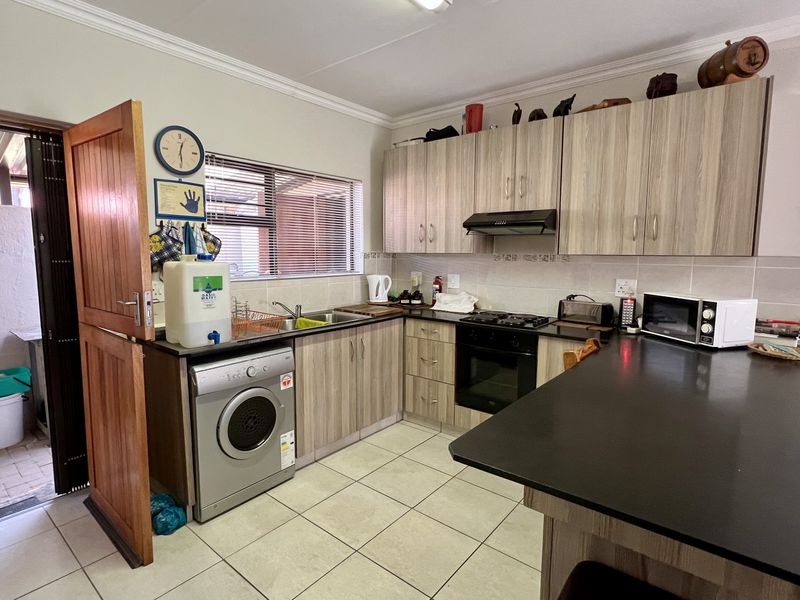 Functional kitchen featuring laminate cabinetry, black stone countertops, built-in oven with gas hob, and integrated laundry space with direct access to an outdoor area.