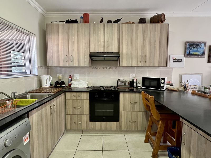 Functional kitchen featuring light wood-grain cabinetry, black countertops, integrated oven and hob, and a convenient breakfast bar for casual dining.