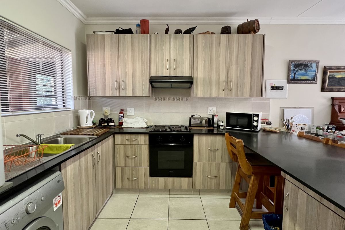 Functional kitchen featuring light wood-grain cabinetry, black countertops, integrated oven and hob, and a convenient breakfast bar for casual dining.
