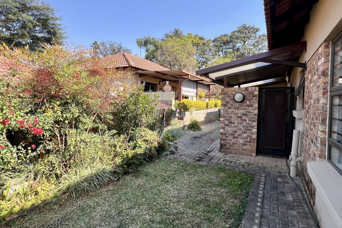 A well-maintained rear exterior view featuring a brick-paved pathway, established garden landscaping, and a covered walkway connecting to the main building structure.