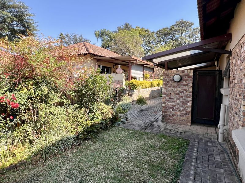 A well-maintained rear exterior view featuring a brick-paved pathway, established garden landscaping, and a covered walkway connecting to the main building structure.
