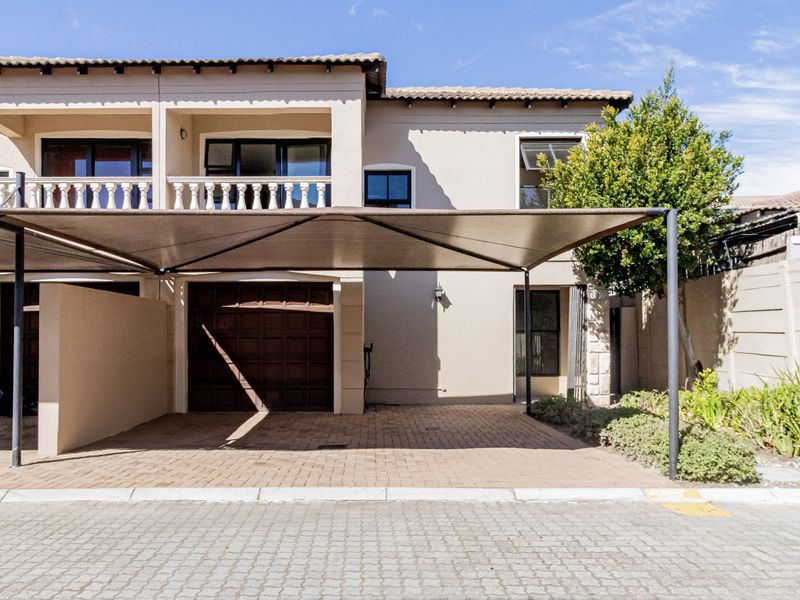 Front elevation of a townhouse featuring a paved driveway, shadeport, integrated garage, and an upper-level balcony with a classic balustrade.