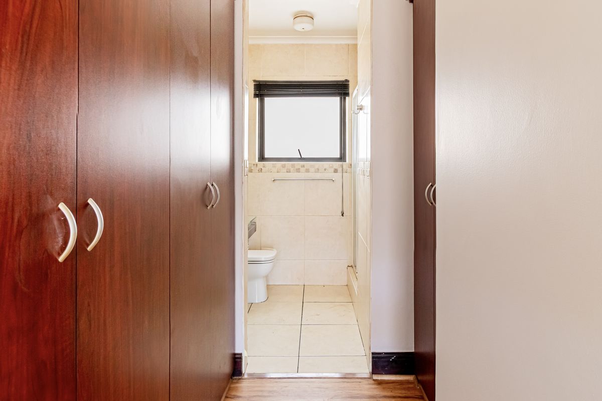 A functional bathroom featuring built-in storage cupboards in the hallway leading to a tiled bathroom area with a shower and toilet.