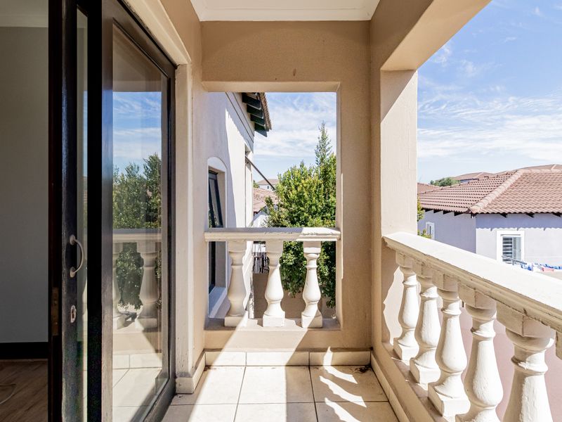 A covered balcony featuring tiled flooring and a classic balustrade, offering an outdoor space accessible via a sliding door.