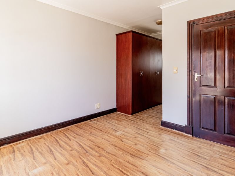 A vacant bedroom featuring laminate flooring, a built-in wardrobe, and a solid timber door.