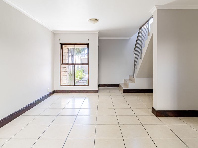 An open-plan living area featuring neutral tiled flooring, a staircase with a metal balustrade, and clean wall finishes.