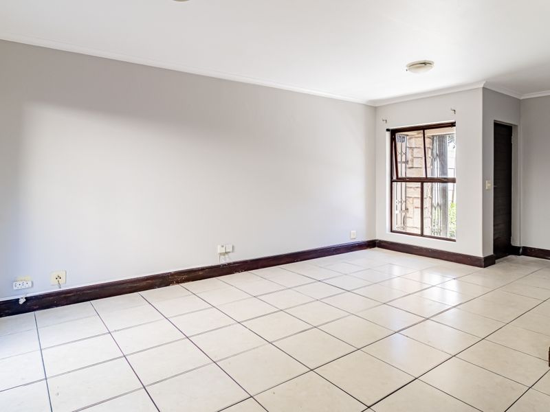A bright, empty living room featuring neutral walls, tiled flooring, and access to an outdoor area through a sliding glass door.