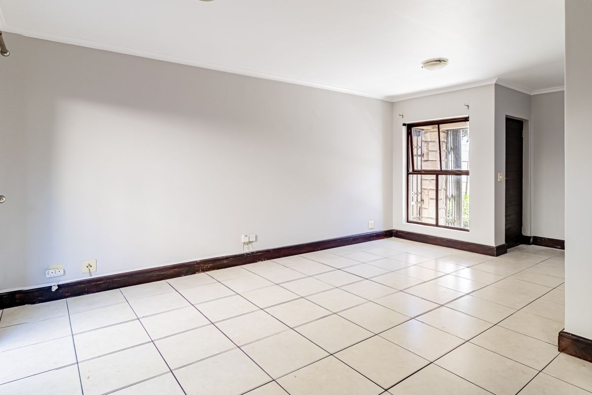 A bright, empty living room featuring neutral walls, tiled flooring, and access to an outdoor area through a sliding glass door.