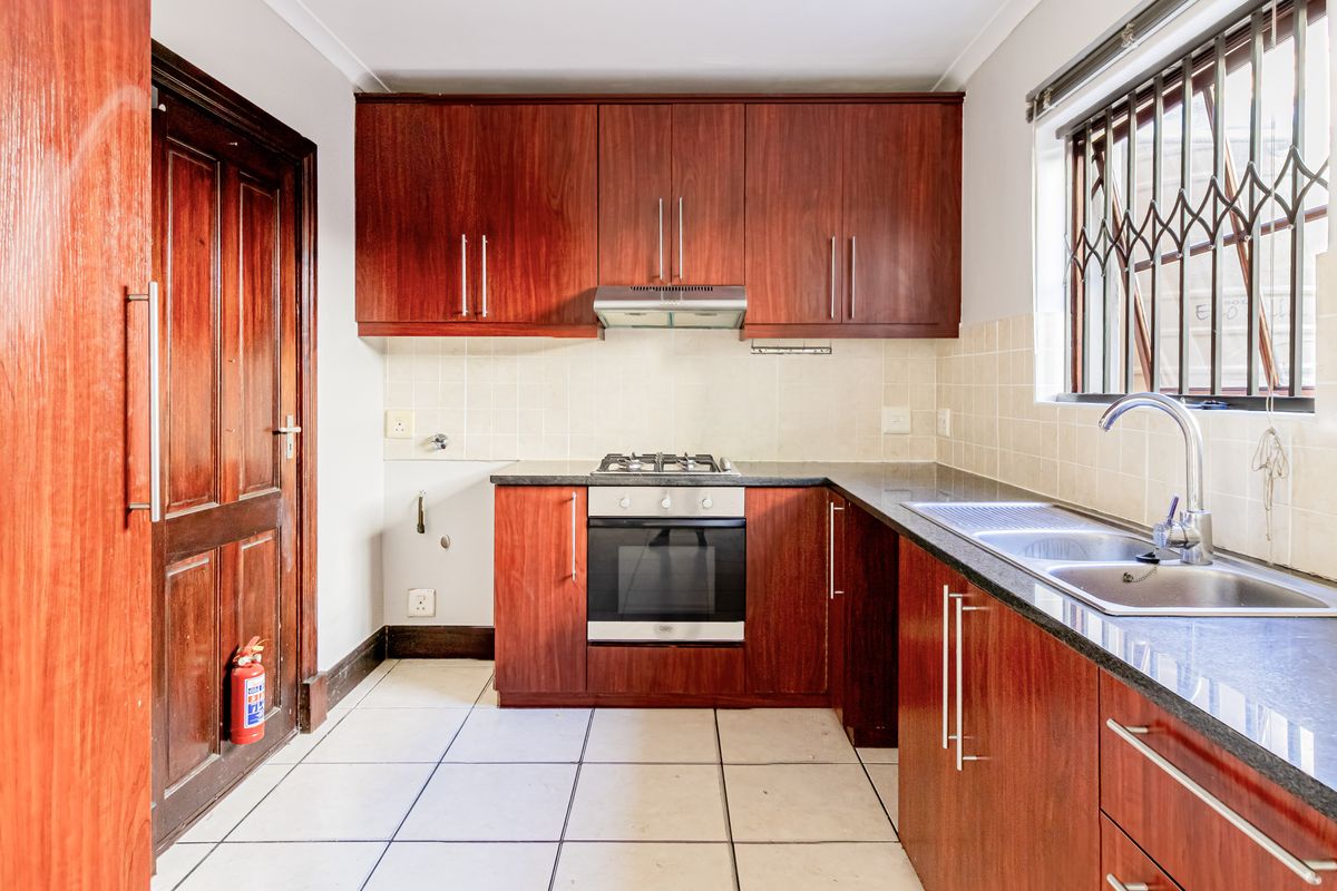 A functional kitchen featuring dark wood cabinetry, a gas hob with oven, double sink, and tiled flooring, offering a clean and practical workspace.