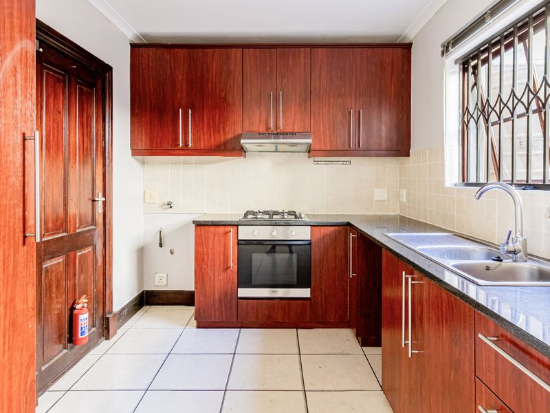 A functional kitchen featuring dark wood cabinetry, a gas hob with oven, double sink, and tiled flooring, offering a clean and practical workspace.