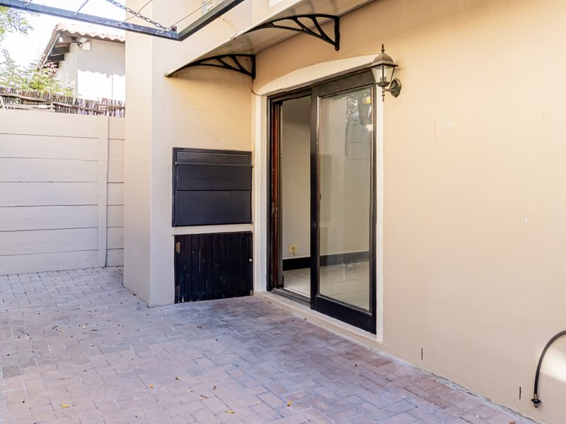 A paved outdoor patio area featuring a built-in braai, sliding door access to the interior, and a protective awning.
