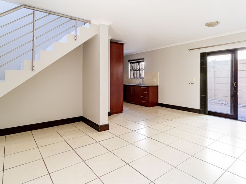 Open-plan living area featuring tiled flooring, a staircase with a stainless steel balustrade, and direct access to an outdoor patio through sliding glass doors.