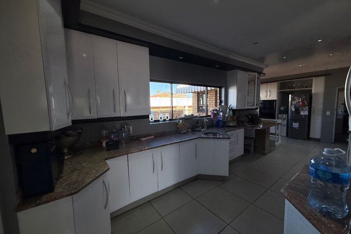 A spacious kitchen featuring white cabinetry, granite countertops, tiled flooring, and ample workspace, with a functional layout and integrated sink.