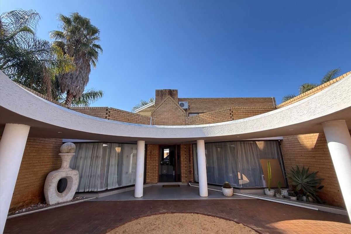 A unique rear exterior view featuring a curved covered patio with concrete columns, brick facade, and a central paved courtyard area.
