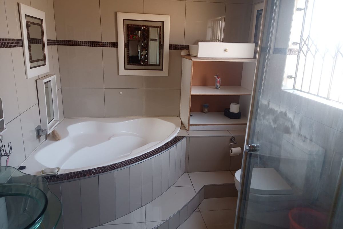 Bathroom featuring a corner bathtub, glass vessel sink, toilet, and shower enclosure with tiled finishes throughout.