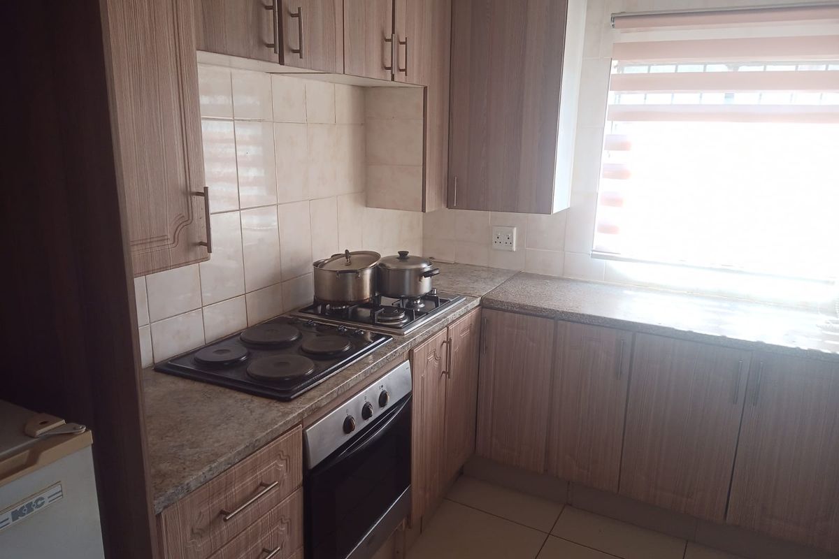 A functional kitchen featuring wood-finish cabinetry, granite countertops, a built-in oven, and an electric hob with a tiled backsplash.