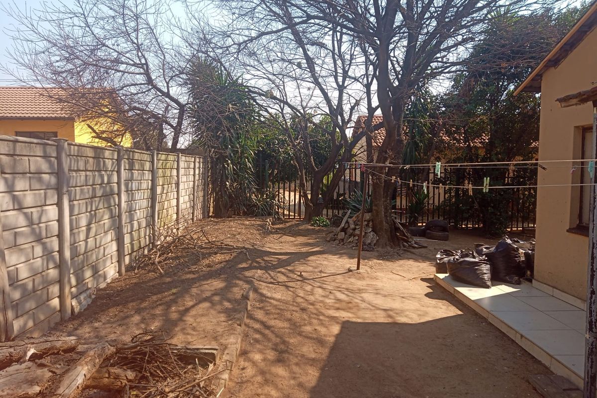 Rear garden area featuring a precast concrete boundary wall, mature trees, and a small tiled patio section.