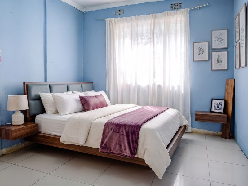 A bedroom featuring tiled flooring and blue walls, with visible wear on the skirting boards and wall base.