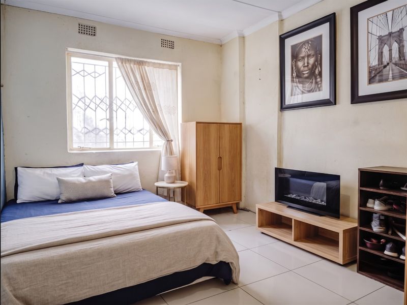 A bedroom featuring tiled flooring, security bars on the window, and built-in ventilation bricks, with visible wear on the wall surfaces.