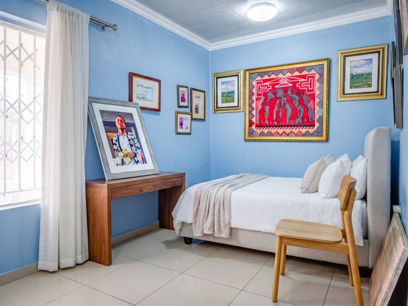 A well-maintained bedroom featuring light blue walls, tiled flooring, and decorative ceiling cornicing, providing a comfortable and bright living space.