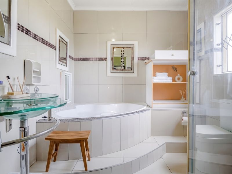 A well-maintained bathroom featuring a built-in corner bathtub, a modern glass vessel sink, and neutral wall tiling with decorative accents.