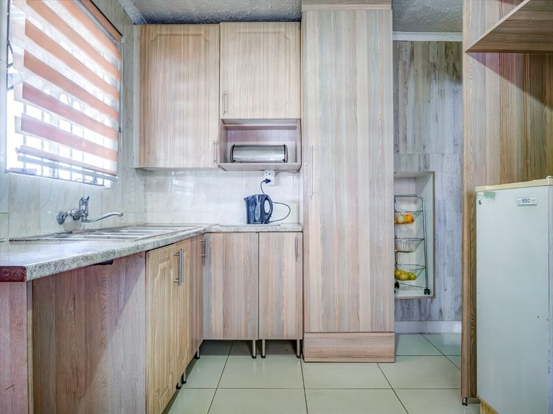 A functional kitchen featuring light wood-look laminate cabinetry, tiled flooring, a stainless steel sink, and ample built-in storage space.
