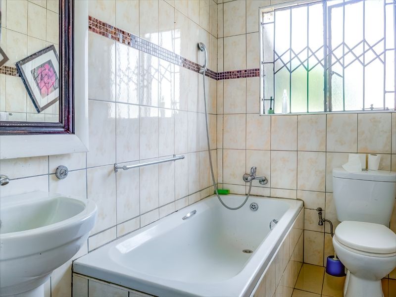 A functional bathroom featuring a bathtub with handheld shower, pedestal basin, and toilet, finished with neutral wall and floor tiles.