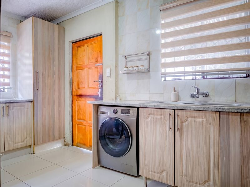 Functional laundry area featuring built-in cabinetry, laminate countertops, a stainless steel sink, and tiled finishes.