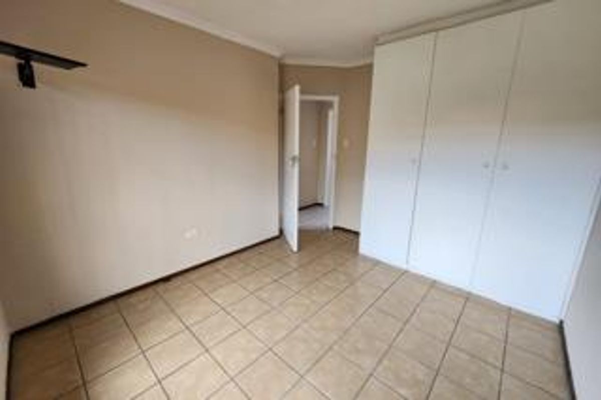A clean, empty bedroom featuring neutral wall tones, tiled flooring, and ample built-in cupboard storage space.