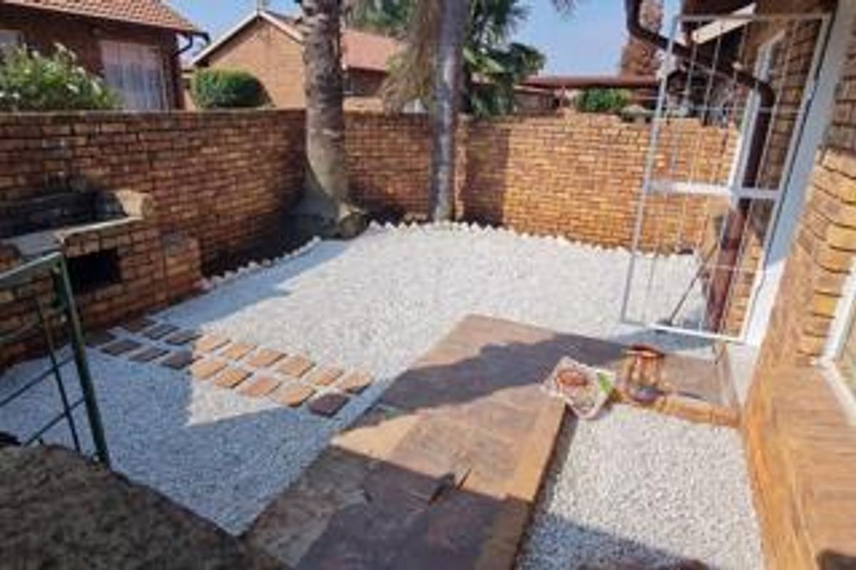 A private rear courtyard featuring a paved patio, built-in braai, and low-maintenance gravel garden enclosed by brick boundary walls.