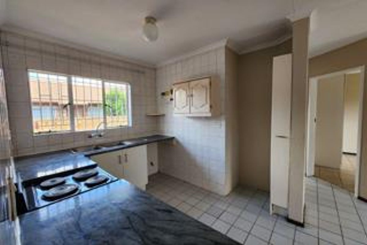 A functional kitchen featuring built-in cabinetry, laminate countertops, a double bowl sink, and an electric hob, finished with tiled splashbacks and flooring.