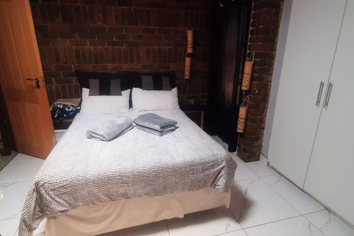 Bedroom featuring an exposed brick feature wall, white tiled flooring, and a built-in wardrobe.