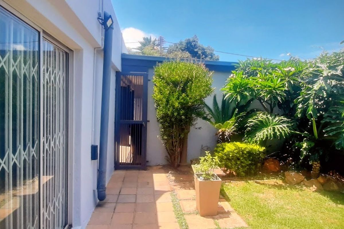 A private rear garden area featuring a paved walkway, established greenery, and access to the home via a sliding glass door with security gate.