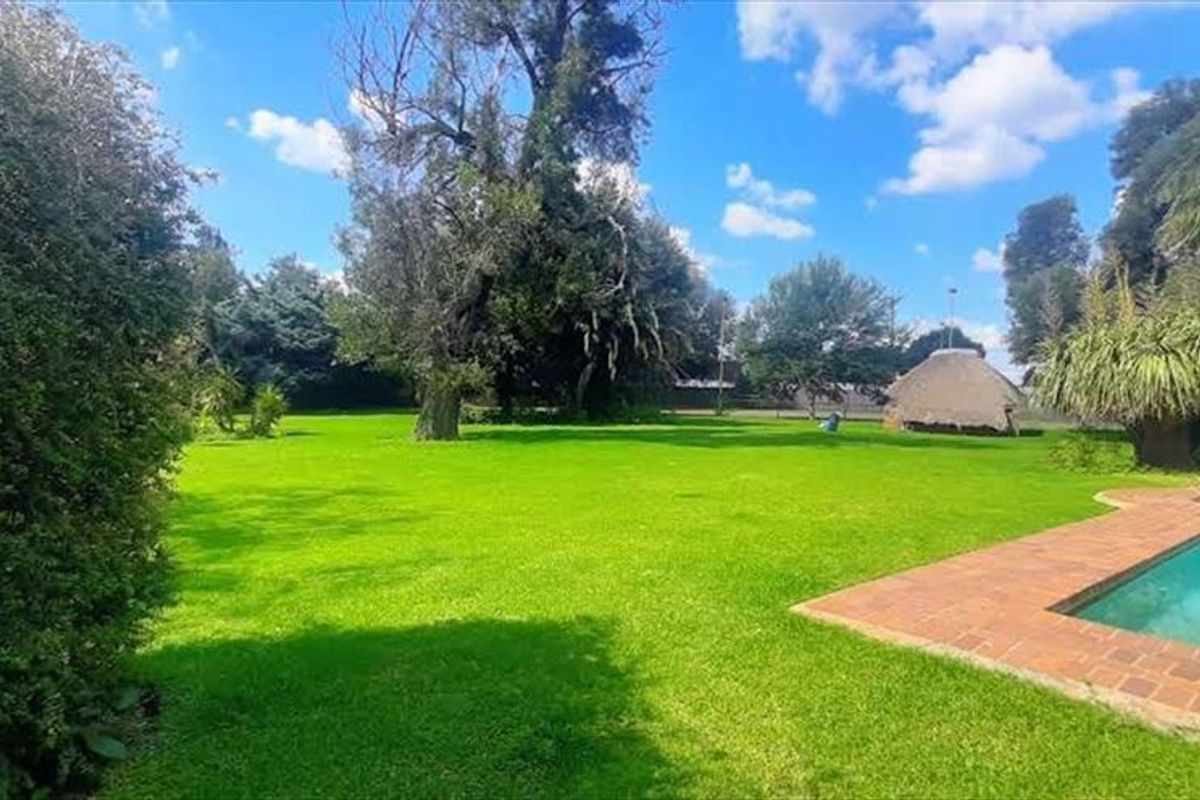 Spacious garden area featuring a swimming pool with brick coping and a traditional thatched lapa in the background.