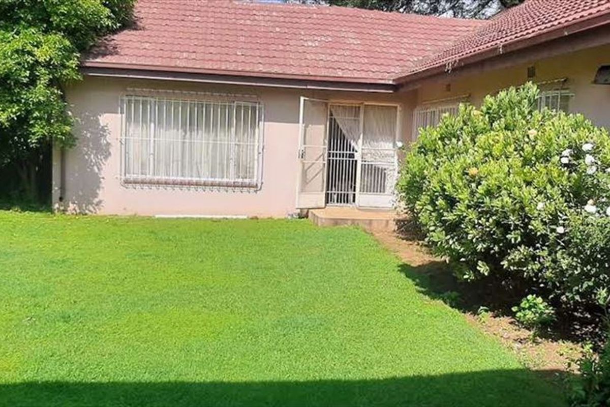 Rear view of the property featuring a well-maintained lawn, tiled roof, and security-fitted windows and doors.