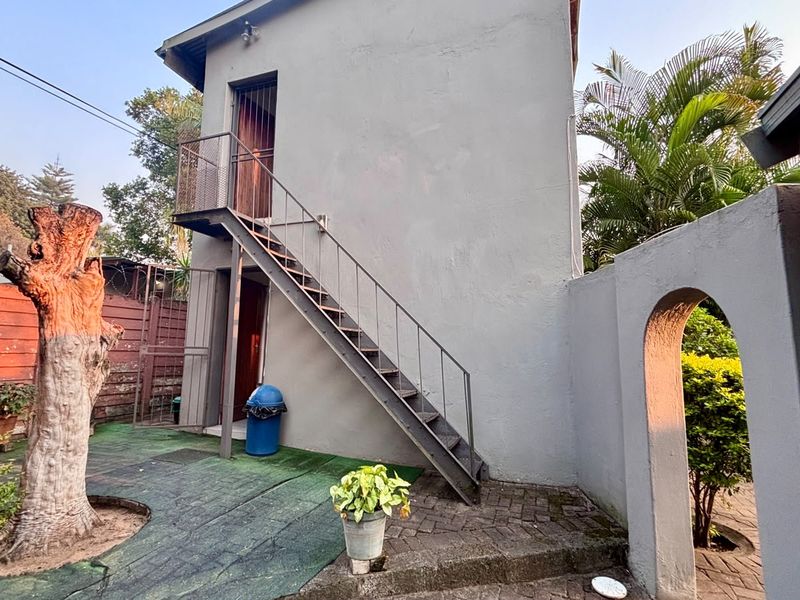 Rear exterior view of the property featuring an external metal staircase, paved courtyard area, and an arched masonry gateway.