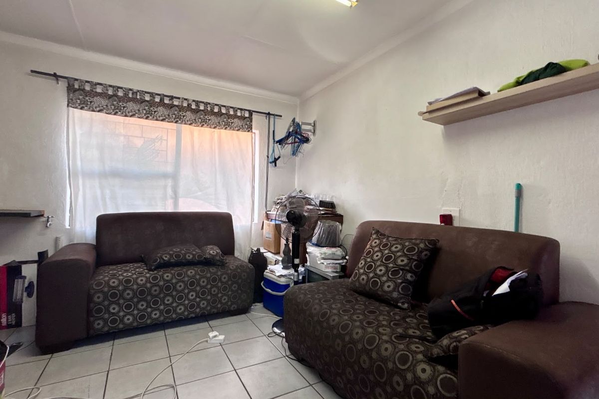 A compact living room featuring tiled flooring and a wall-mounted shelf, requiring cosmetic updates to improve its overall appeal and condition.