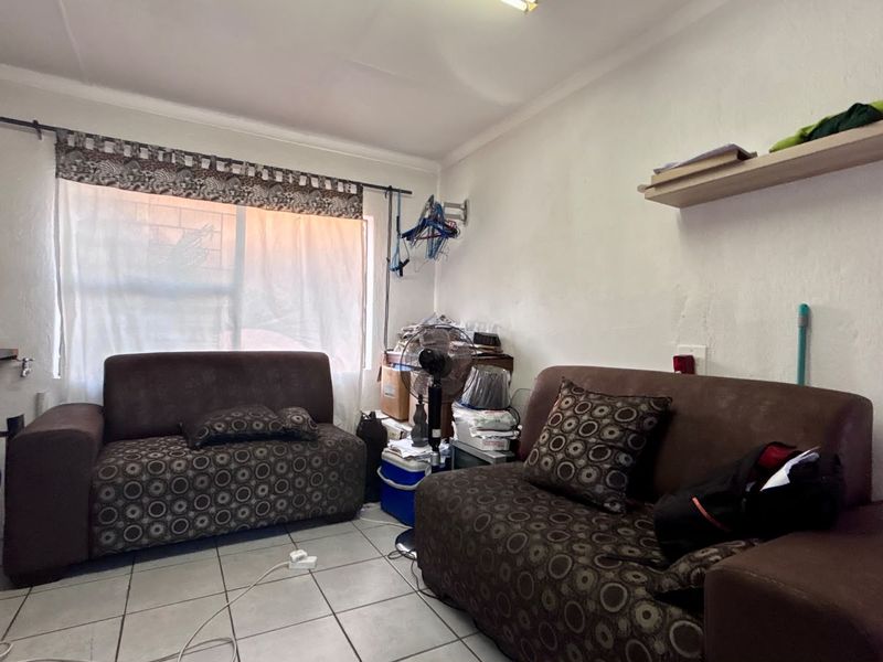 A compact living room featuring tiled flooring and a wall-mounted shelf, requiring cosmetic updates to improve its overall appeal and condition.