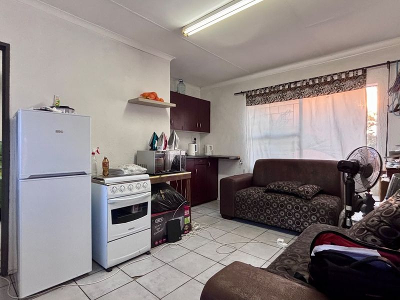 Open-plan living area featuring tiled flooring and a compact kitchen space with built-in cabinetry and a freestanding stove.