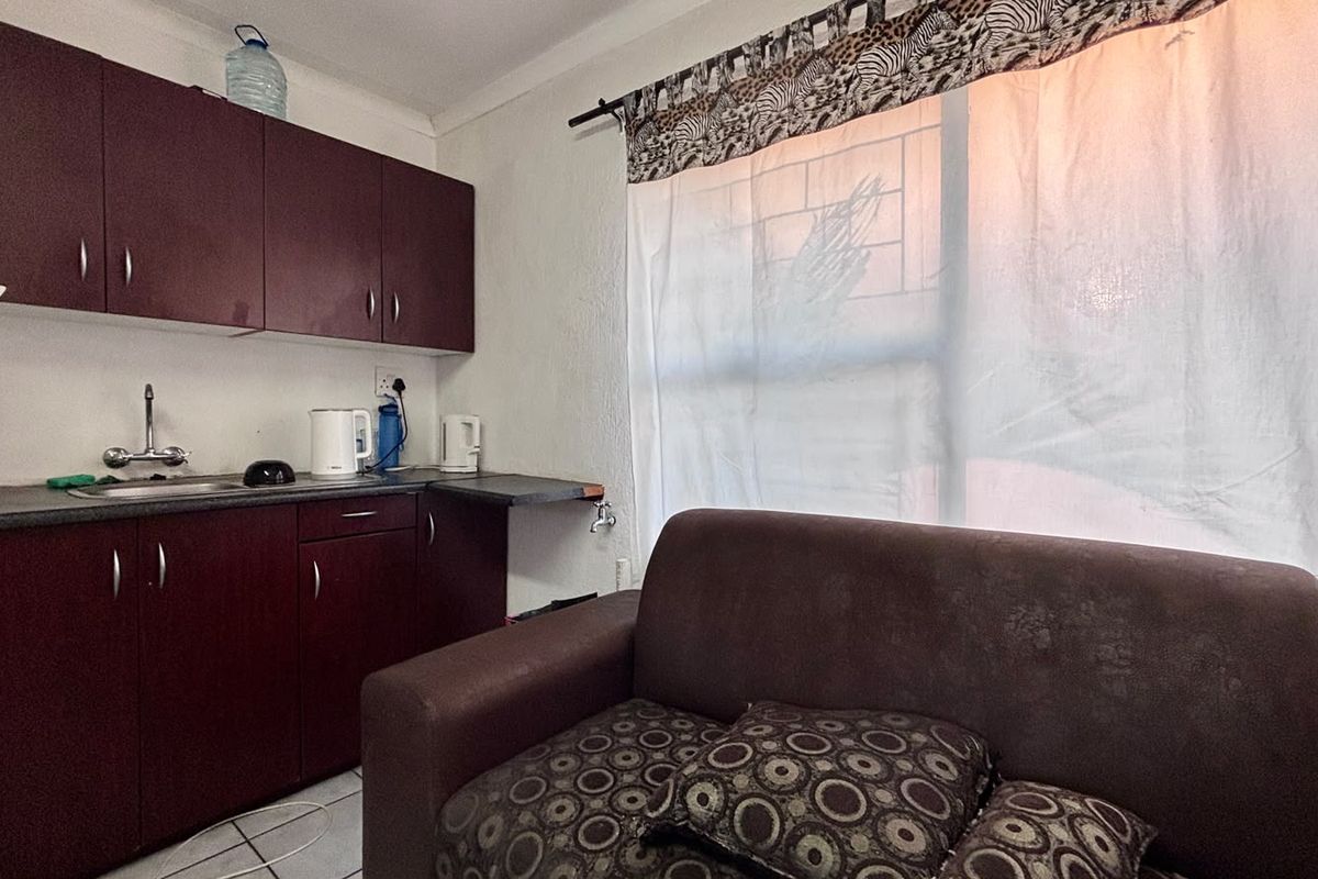 Compact open-plan living area featuring a kitchenette with laminate cabinetry, stainless steel sink, and tiled flooring, suitable for efficient apartment living.