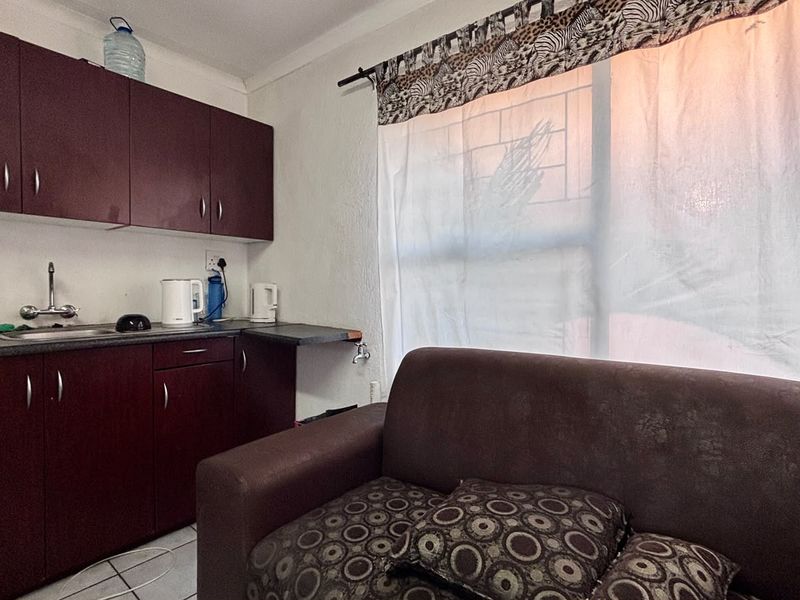Compact open-plan living area featuring a kitchenette with laminate cabinetry, stainless steel sink, and tiled flooring, suitable for efficient apartment living.