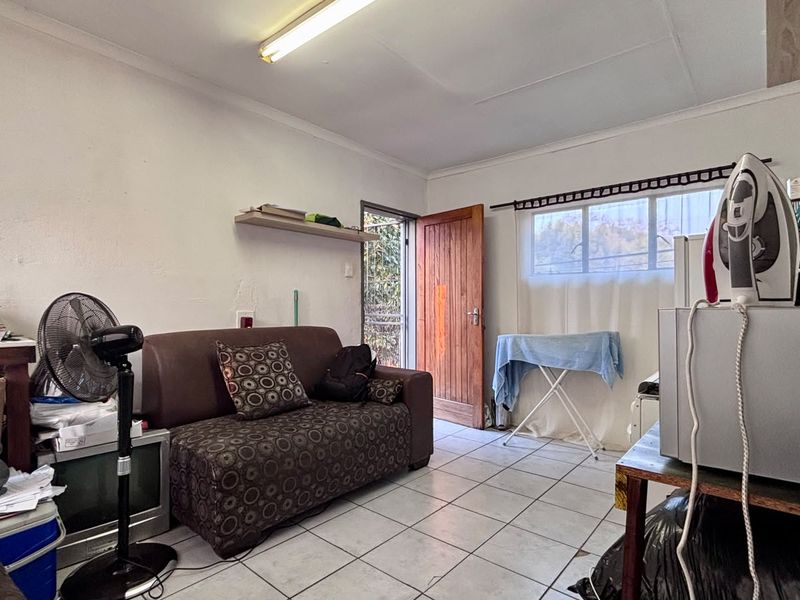 A living area featuring tiled flooring, a timber entrance door, and a window, providing a functional space with potential for cosmetic updates.