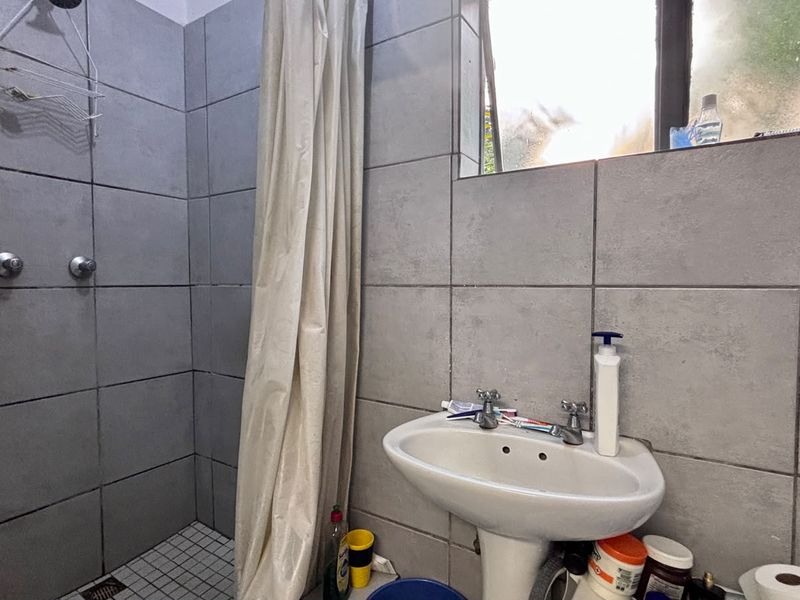A compact bathroom featuring grey wall tiles, a pedestal basin, and a shower area with a curtain.