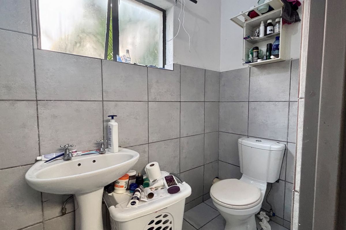 A functional bathroom featuring a pedestal basin, toilet, and grey tiled walls. The space would benefit from cosmetic updates and improved storage solutions.
