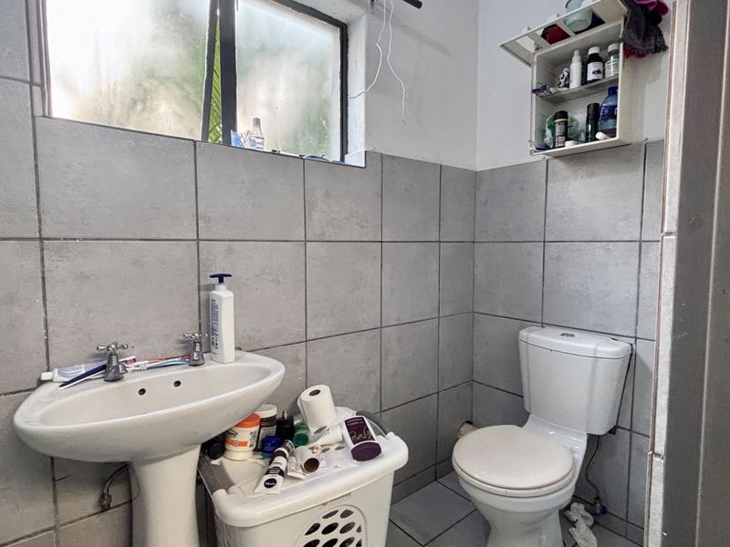 A functional bathroom featuring a pedestal basin, toilet, and grey tiled walls. The space would benefit from cosmetic updates and improved storage solutions.