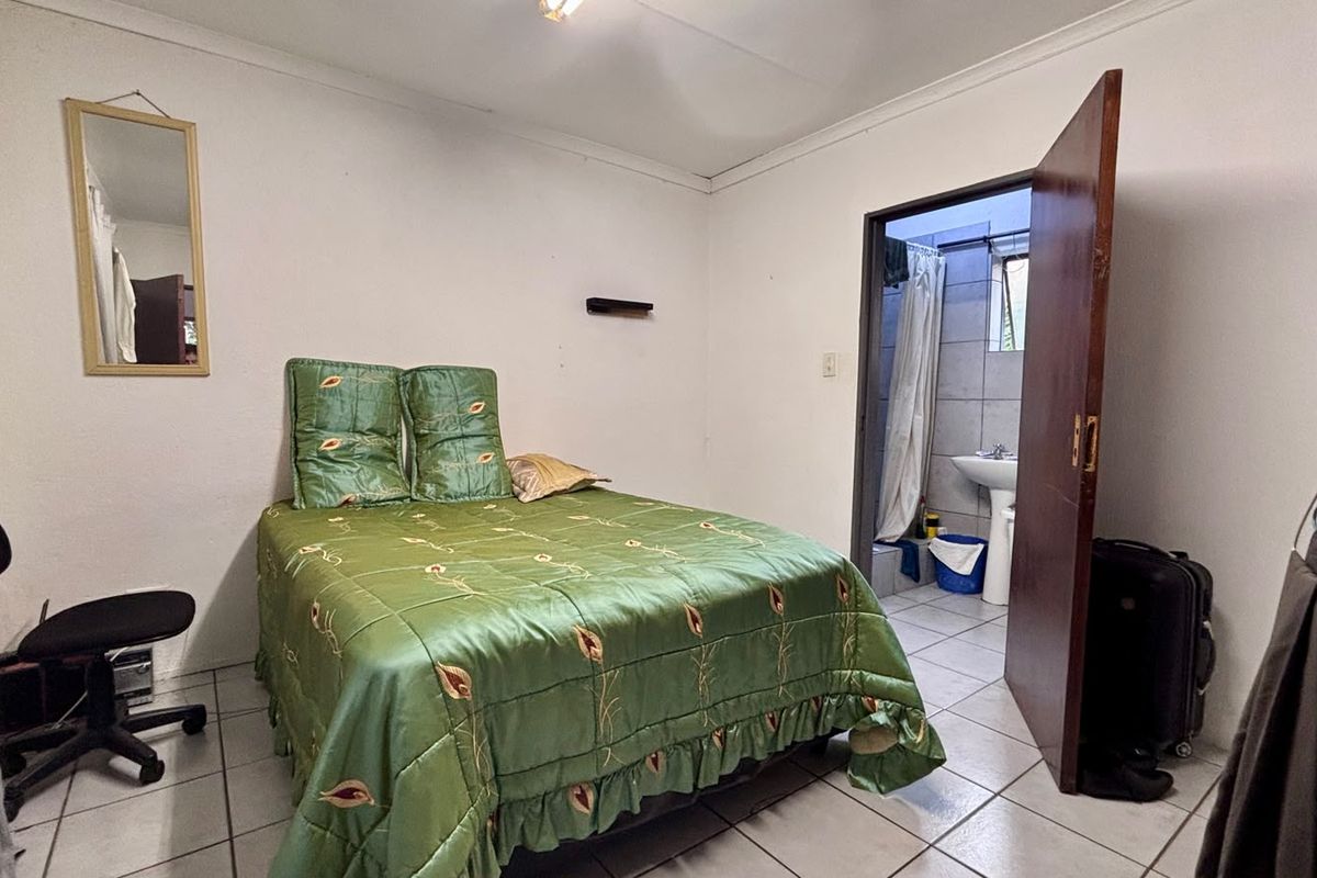 A bedroom featuring tiled flooring and an attached en-suite bathroom with a pedestal basin and shower.