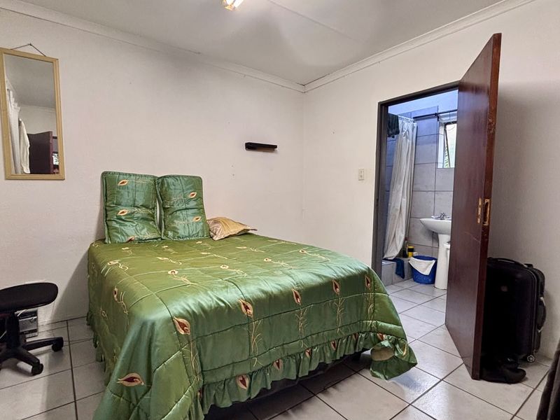 A bedroom featuring tiled flooring and an attached en-suite bathroom with a pedestal basin and shower.