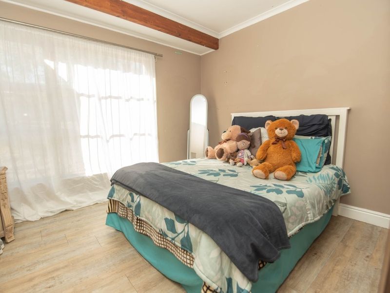 A bedroom featuring laminate wood flooring, an exposed timber ceiling beam, and a built-in wardrobe, offering a functional space with neutral wall tones.