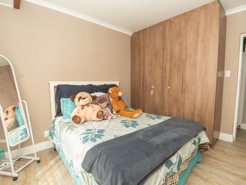 A bedroom featuring laminate flooring and a large built-in wooden wardrobe with visible wear on the wall surfaces.