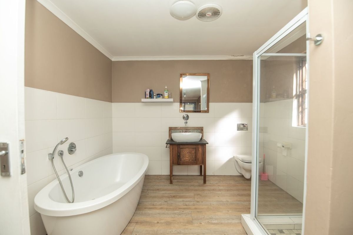 A functional bathroom featuring a freestanding bathtub, a separate shower enclosure, a wall-mounted toilet, and a wooden vanity with a vessel sink.